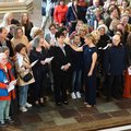 Eine Gruppe von Menschen steht im Altarraum einer Kirche. In der Mitte wird eine Frau gesegnet. Die Menschen legen jeweils eine Hand auf die Schulter ihrer Nachbarn.